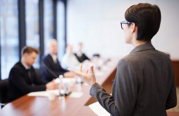 Back view portrait of young businesswoman giving speech in conference room and gesturing, copy space