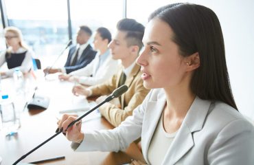Serious confident attractive female politician speaking into microphone and amplifying voice of her country at international meeting
