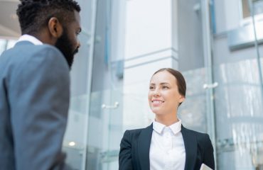 Smiling attractive young manager with tablet making handshake with Black investor while meeting him in office hall